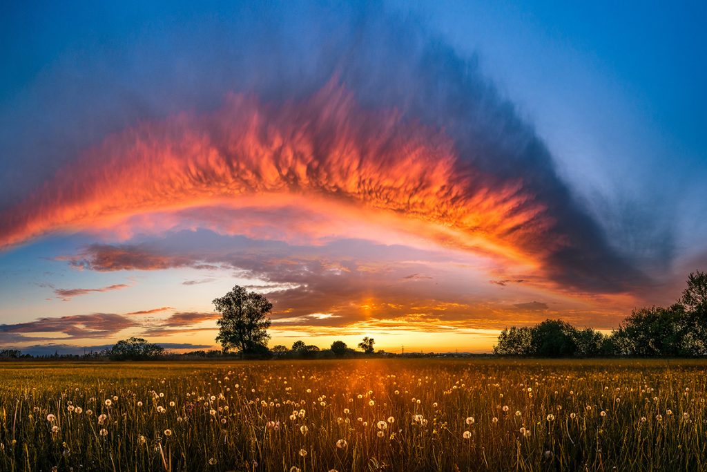 Spektakuläres Wolkenband wird von der untergehenden Sonne rot beleuchtet
